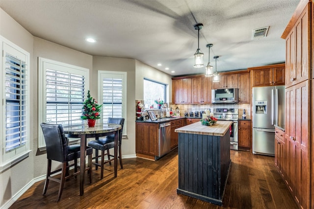 kitchen with wood counters, a center island, dark hardwood / wood-style floors, appliances with stainless steel finishes, and decorative light fixtures