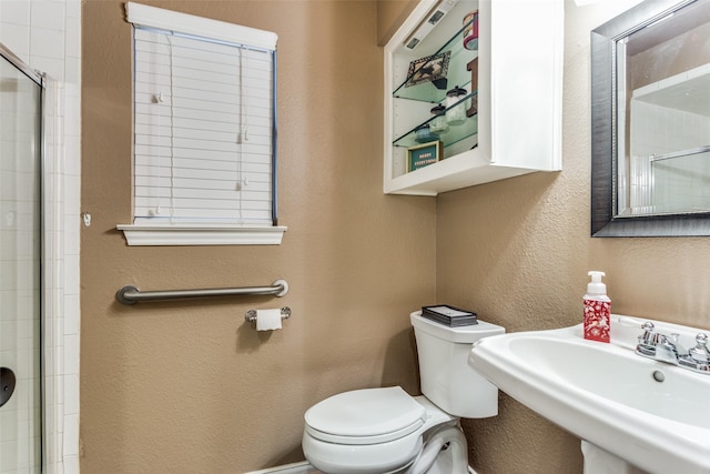 bathroom with sink, a shower with shower door, and toilet