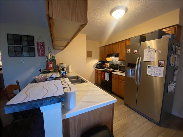 kitchen featuring electric range, sink, a kitchen breakfast bar, stainless steel fridge, and a textured ceiling