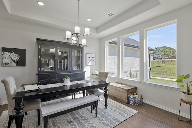 dining area featuring an inviting chandelier, a tray ceiling, and dark hardwood / wood-style flooring