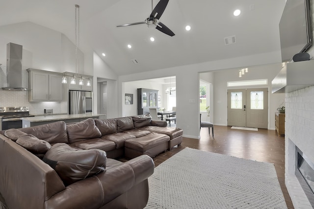 living room featuring ceiling fan with notable chandelier, a fireplace, high vaulted ceiling, and dark hardwood / wood-style floors