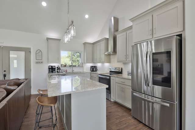 kitchen with light stone countertops, appliances with stainless steel finishes, wall chimney range hood, a kitchen island, and lofted ceiling