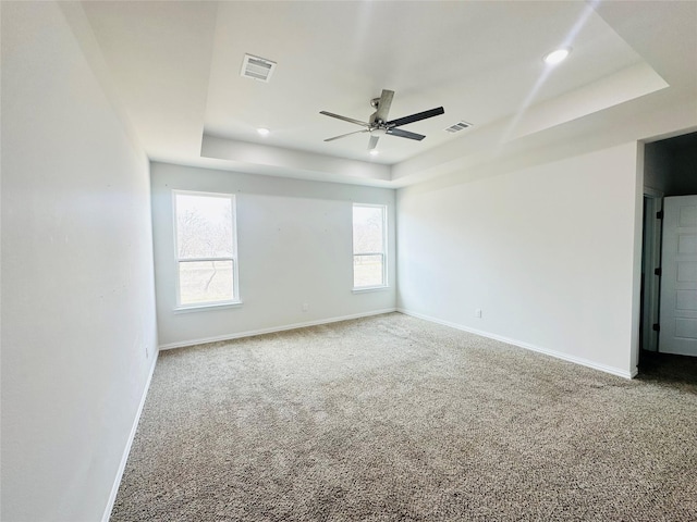 carpeted empty room with a raised ceiling and ceiling fan