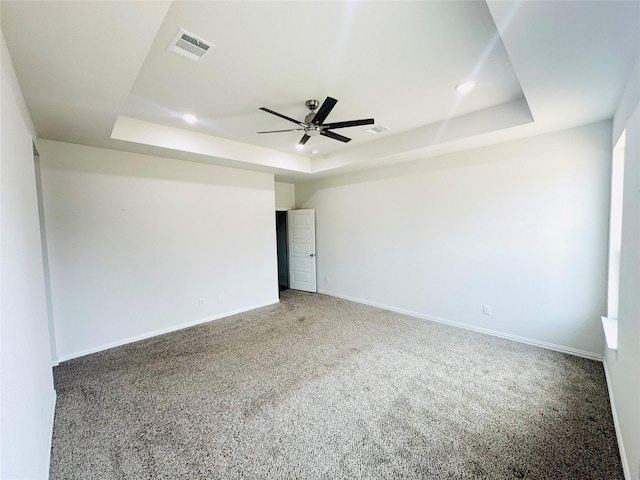 spare room featuring a raised ceiling, carpet, and ceiling fan