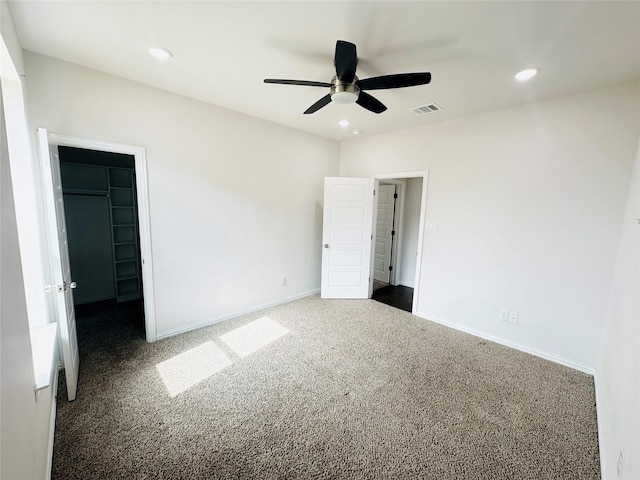 unfurnished bedroom featuring dark colored carpet, a walk in closet, ceiling fan, and a closet