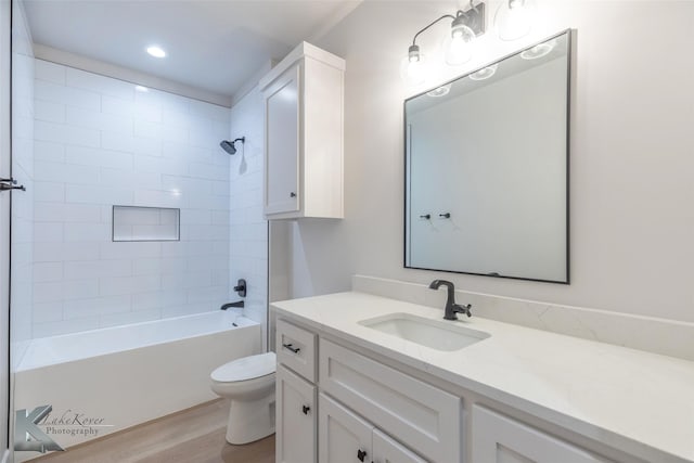 full bathroom featuring wood-type flooring, tiled shower / bath, vanity, and toilet