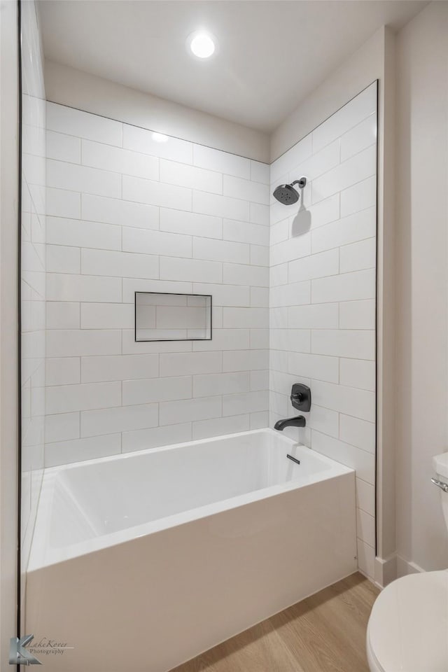 bathroom featuring wood-type flooring, tiled shower / bath, and toilet