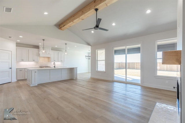 kitchen with white cabinetry, lofted ceiling with beams, hanging light fixtures, an island with sink, and light hardwood / wood-style floors