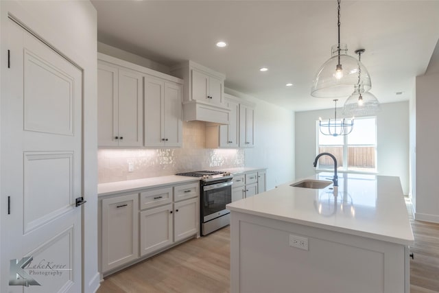 kitchen with white cabinetry, a kitchen island with sink, sink, and stainless steel gas stove