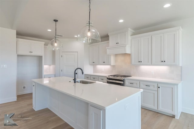 kitchen featuring white cabinets, sink, stainless steel range with gas stovetop, and a kitchen island with sink