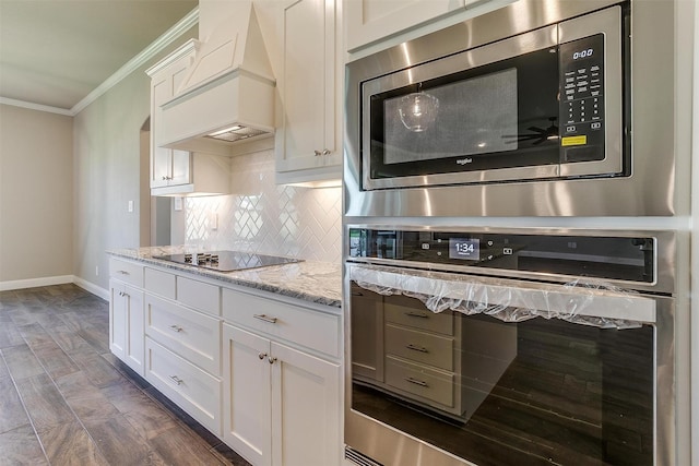 kitchen featuring light stone countertops, premium range hood, appliances with stainless steel finishes, white cabinets, and ornamental molding