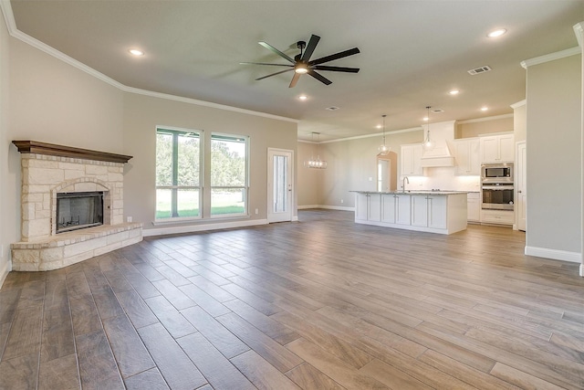 unfurnished living room featuring ornamental molding, light hardwood / wood-style flooring, ceiling fan, and a stone fireplace