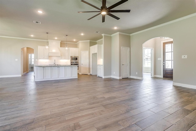 unfurnished living room with ceiling fan, light hardwood / wood-style floors, sink, and crown molding