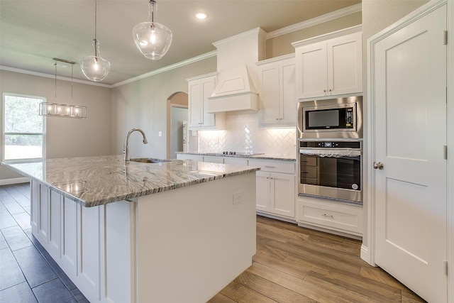 kitchen featuring a center island with sink, white cabinets, hanging light fixtures, and appliances with stainless steel finishes