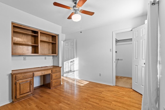 unfurnished office featuring built in desk, light hardwood / wood-style flooring, and ceiling fan