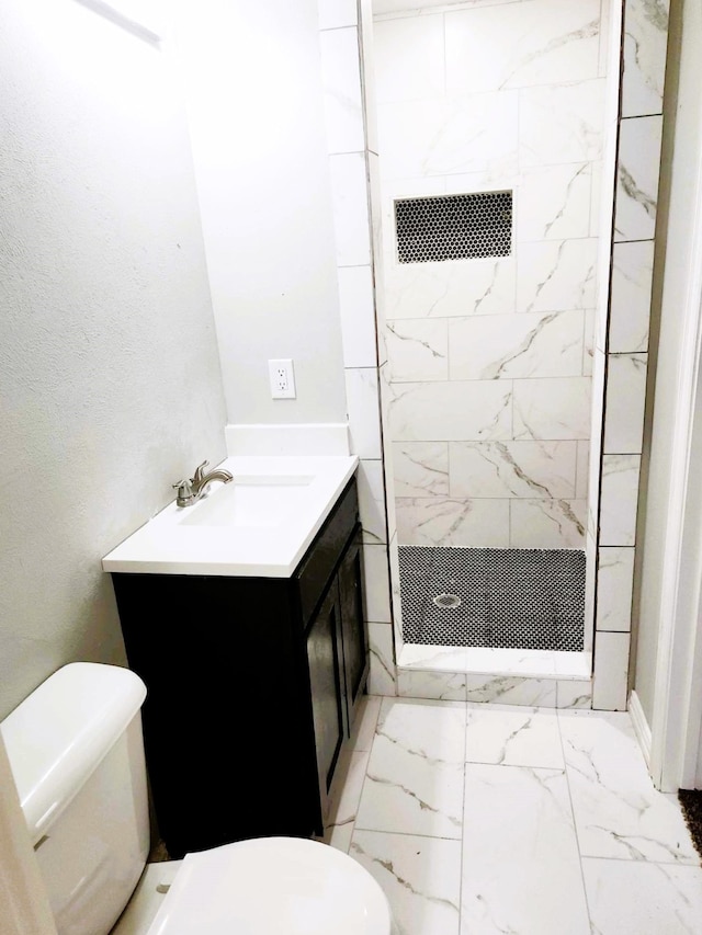 bathroom featuring vanity, a tile shower, and toilet