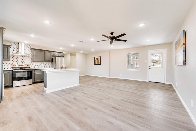 kitchen with wall chimney range hood, light hardwood / wood-style flooring, appliances with stainless steel finishes, gray cabinetry, and a kitchen island