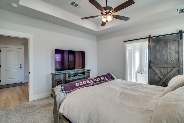 bedroom featuring light carpet, a barn door, ensuite bath, and ceiling fan