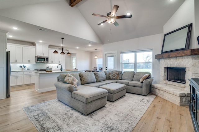 living room featuring high vaulted ceiling, sink, light hardwood / wood-style flooring, ceiling fan, and a fireplace