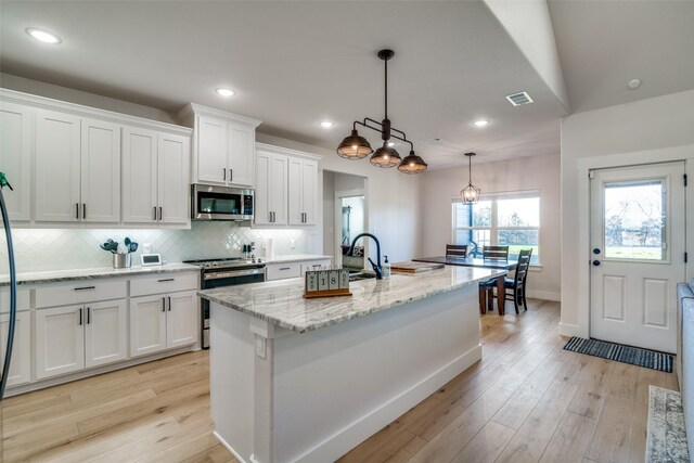 kitchen featuring appliances with stainless steel finishes, light wood-type flooring, pendant lighting, a center island with sink, and white cabinets