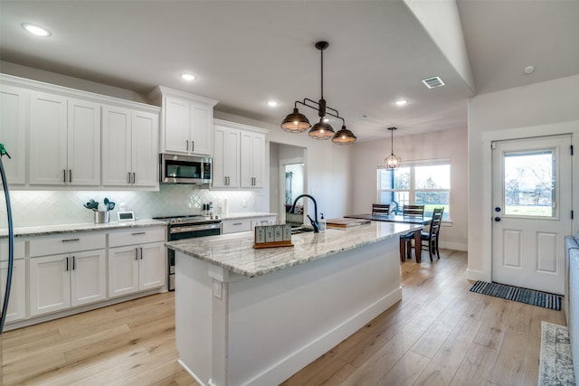 kitchen with pendant lighting, white cabinetry, a kitchen island with sink, light stone counters, and stainless steel appliances