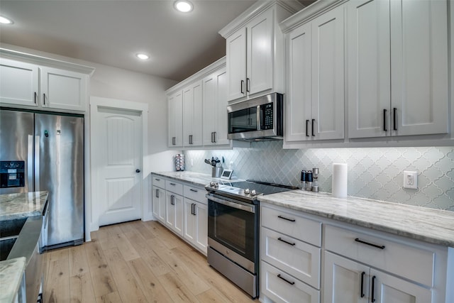 kitchen with white cabinets, appliances with stainless steel finishes, light wood-type flooring, and light stone counters