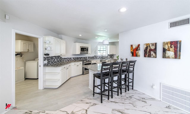 kitchen featuring a breakfast bar area, white cabinetry, stainless steel appliances, decorative backsplash, and washer / dryer