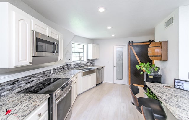 kitchen with white cabinetry, sink, light stone counters, stainless steel appliances, and a barn door