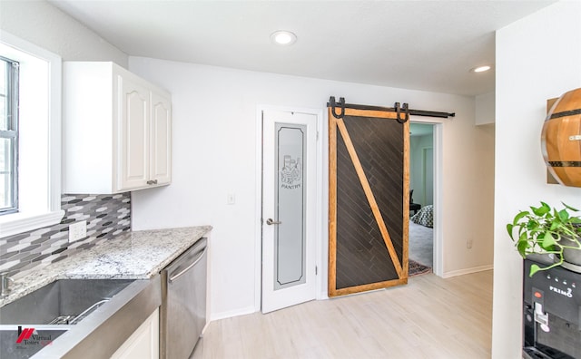 kitchen with a wealth of natural light, a barn door, stainless steel dishwasher, and white cabinets