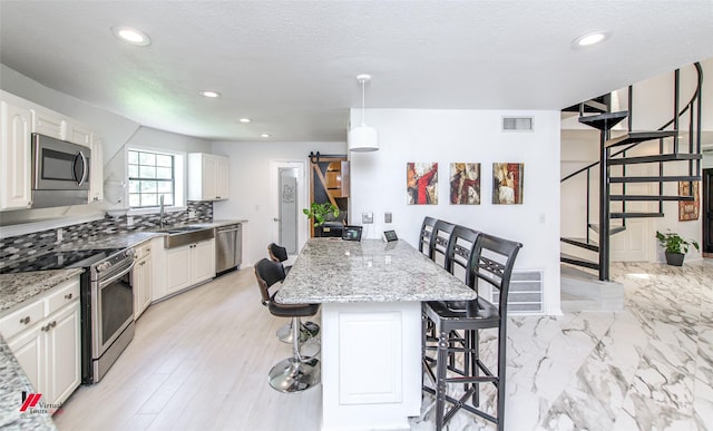 kitchen featuring appliances with stainless steel finishes, a barn door, a breakfast bar, and light stone countertops