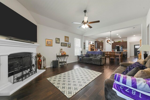 living room featuring ceiling fan with notable chandelier, dark wood-type flooring, and vaulted ceiling