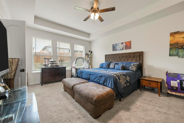 bedroom featuring light carpet, a tray ceiling, and ceiling fan