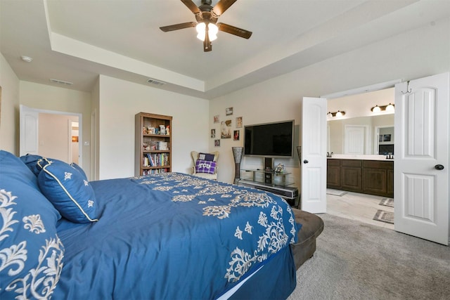 bedroom featuring light carpet, connected bathroom, a raised ceiling, and ceiling fan