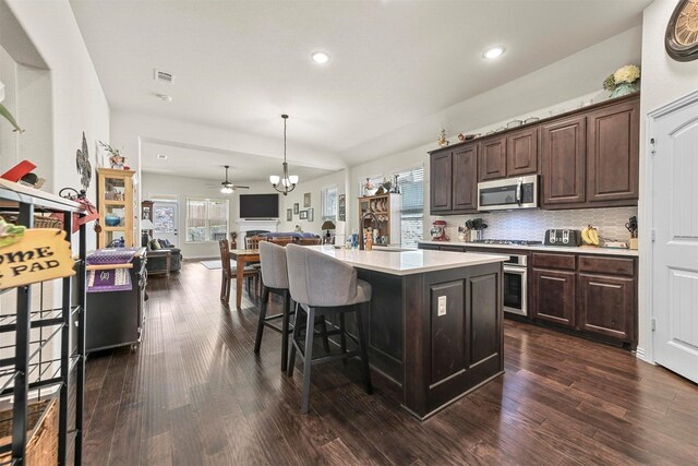 kitchen featuring a center island with sink, dark brown cabinets, dark wood-type flooring, and appliances with stainless steel finishes