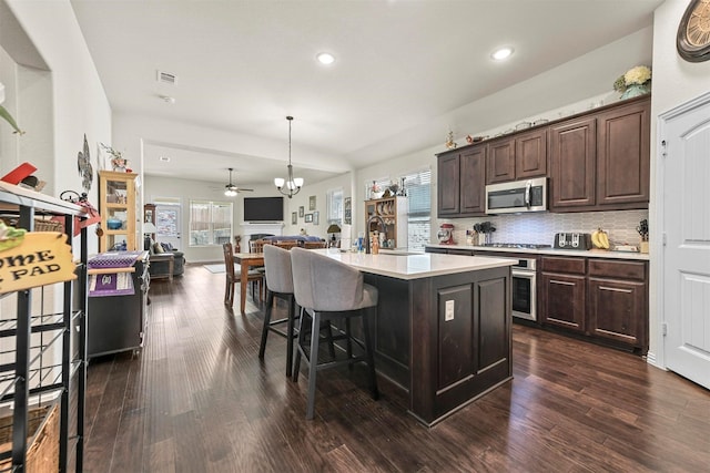 kitchen featuring stainless steel appliances, pendant lighting, dark brown cabinets, and a center island with sink