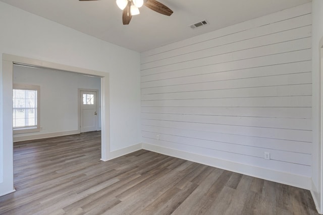 empty room with ceiling fan, light wood-type flooring, and wood walls