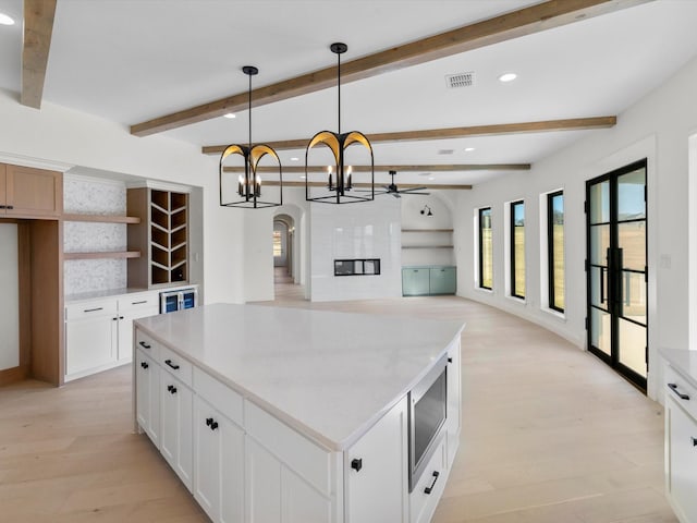 kitchen with white cabinetry, stainless steel microwave, a center island, beamed ceiling, and pendant lighting