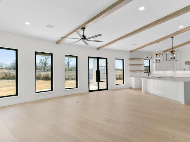 unfurnished living room with ceiling fan with notable chandelier, beam ceiling, and light hardwood / wood-style flooring