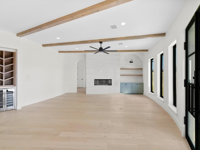 unfurnished living room featuring a tile fireplace, beam ceiling, light wood-type flooring, and ceiling fan