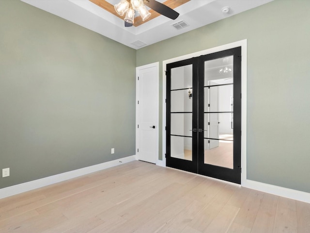 spare room featuring a raised ceiling, ceiling fan, light hardwood / wood-style flooring, and french doors