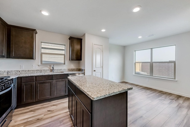 kitchen with stove, sink, a kitchen island, light stone countertops, and light hardwood / wood-style floors