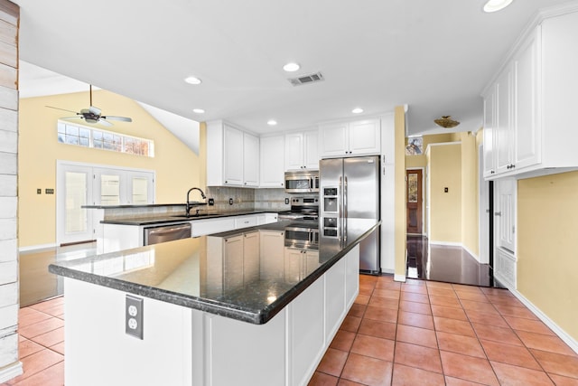 kitchen with a center island, light tile patterned flooring, vaulted ceiling, white cabinets, and appliances with stainless steel finishes