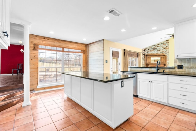 kitchen featuring decorative backsplash, wooden walls, sink, white cabinets, and a kitchen island