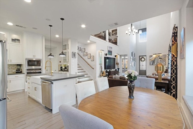 dining space with a high ceiling, sink, a notable chandelier, and light wood-type flooring