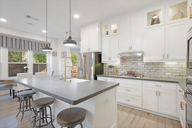 kitchen featuring a center island with sink, sink, hanging light fixtures, appliances with stainless steel finishes, and a breakfast bar area