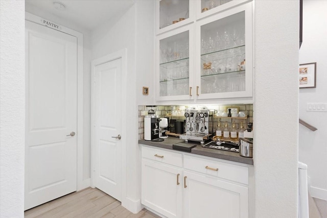 bar with white cabinetry, decorative backsplash, and light hardwood / wood-style floors