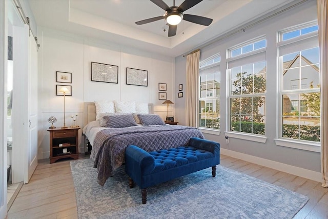 bedroom featuring ceiling fan, light wood-type flooring, and a tray ceiling