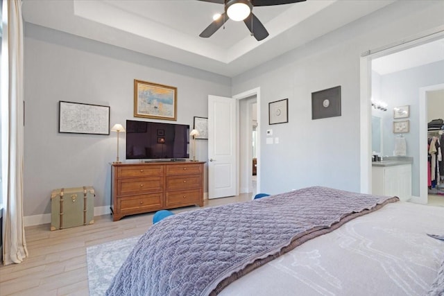 bedroom with ceiling fan, ensuite bathroom, light hardwood / wood-style floors, and a tray ceiling