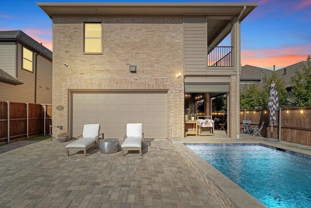 back house at dusk with a balcony, a fenced in pool, and a patio