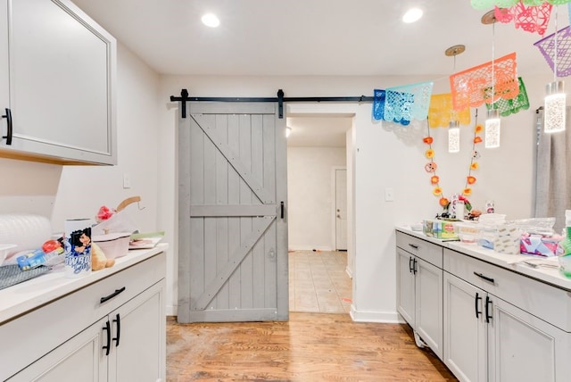 kitchen with decorative light fixtures, a barn door, light wood-type flooring, and white cabinetry